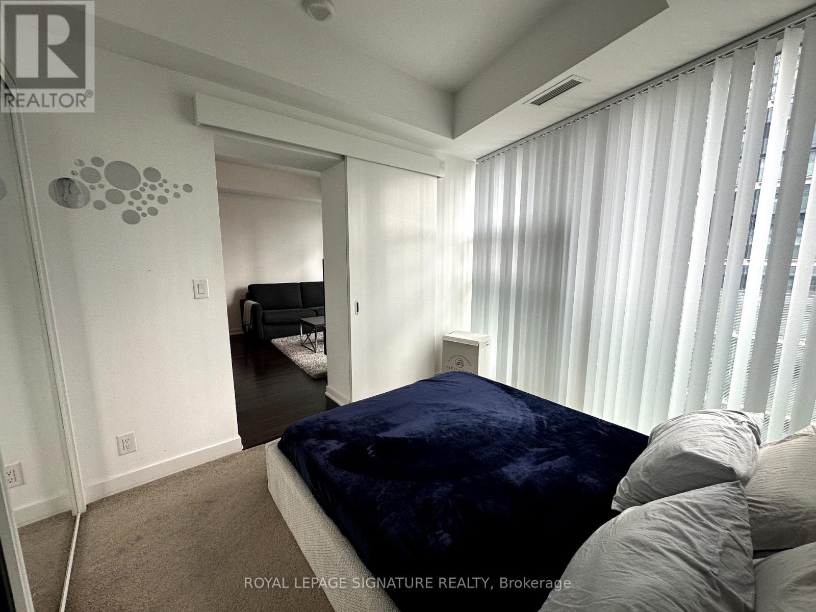 A bedroom with a bed covered in a blue velvet bedspread and a carpeted floor.