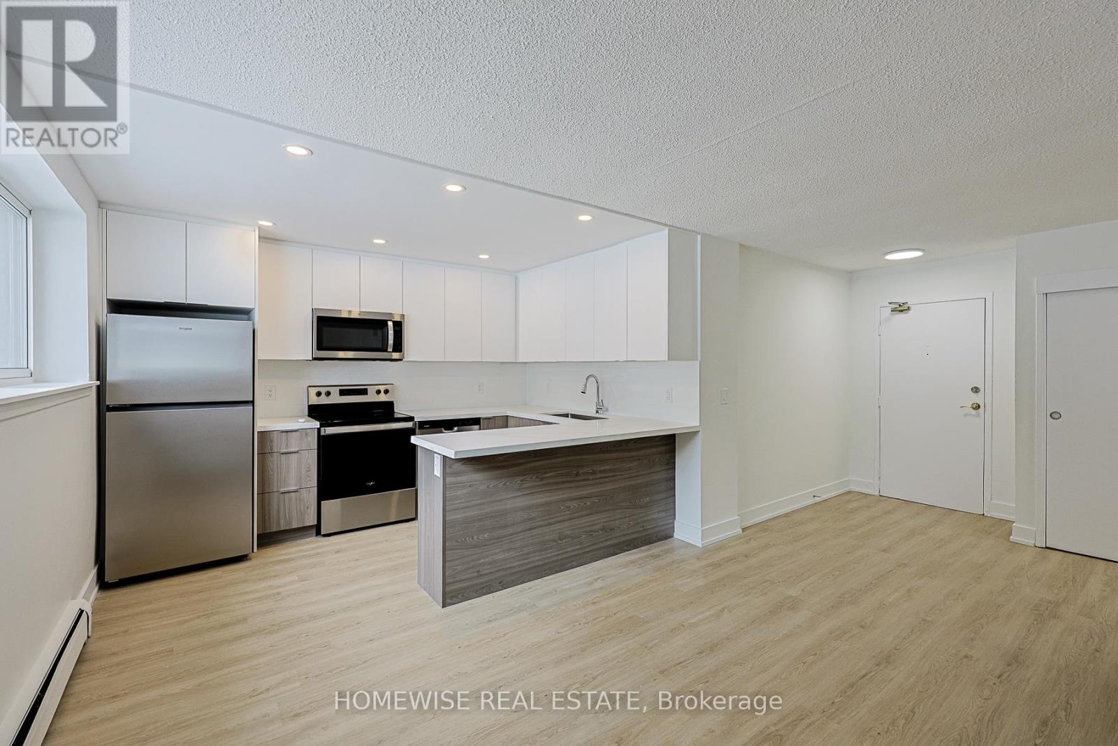 A kitchen with a refrigerator, microwave, oven, and sink.