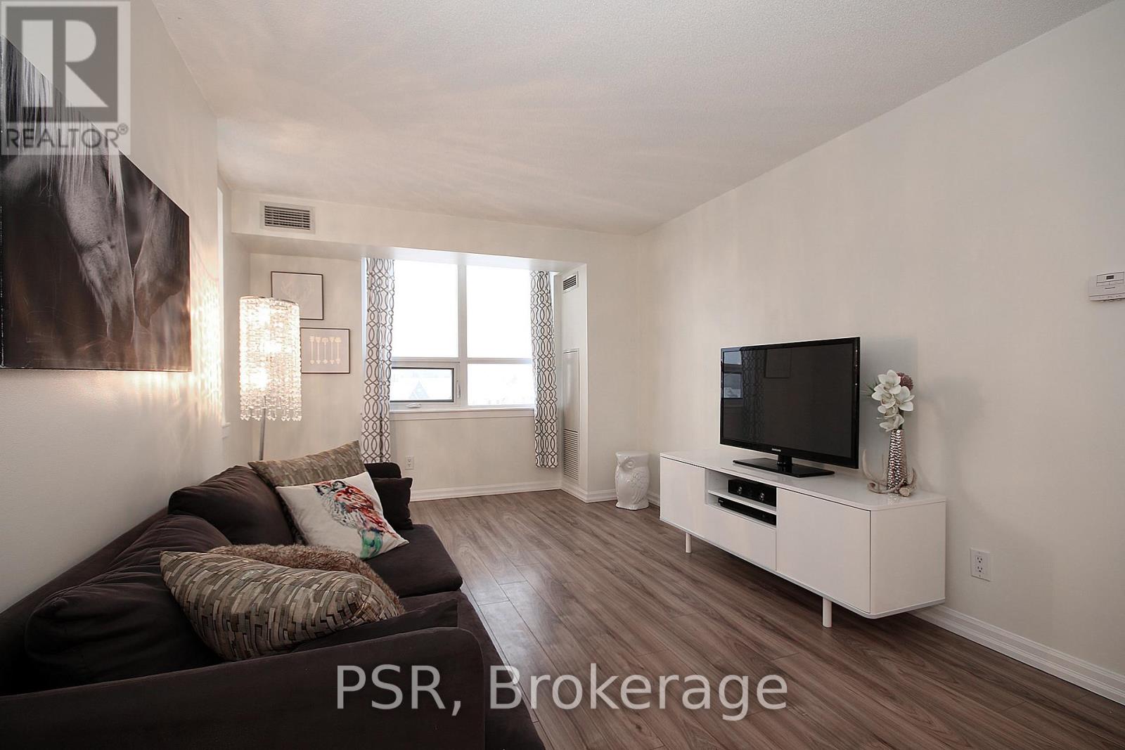 A living room with a brown couch and a television on a white stand.