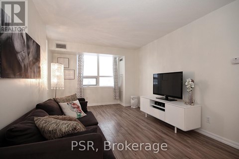 A living room with a brown couch and a television on a white stand.