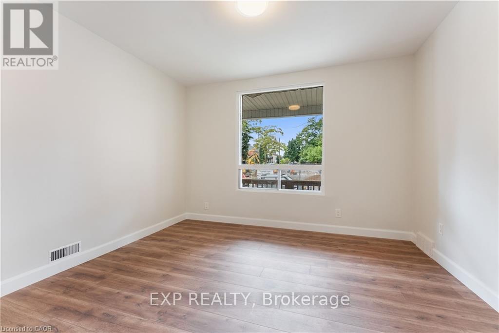 A room with wooden flooring and a window showing a view of trees and a house.