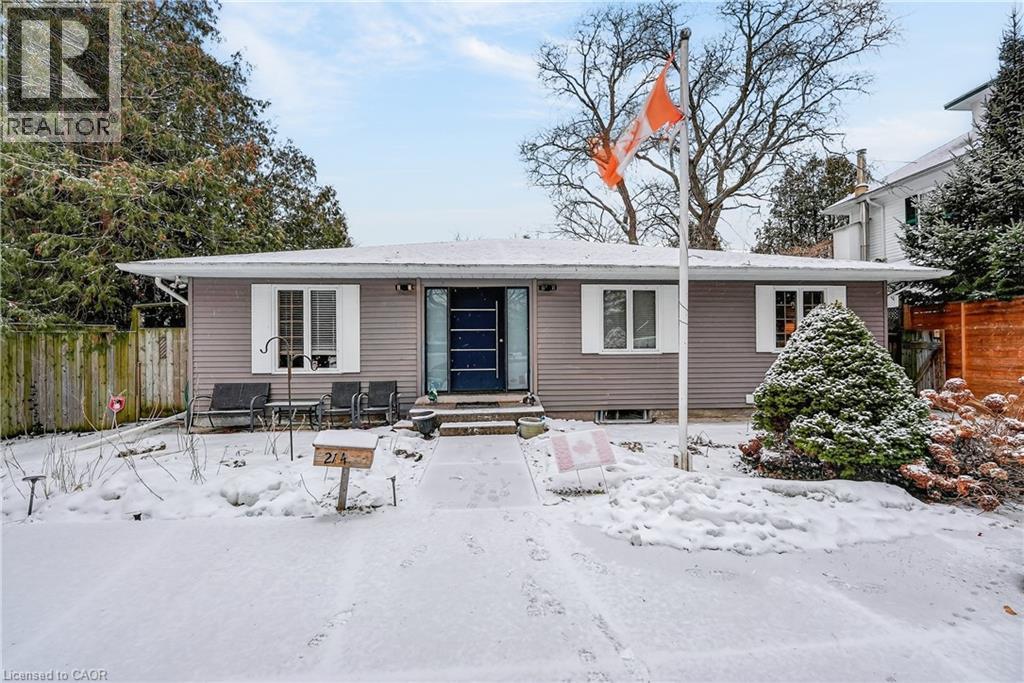 A house with a grey exterior and a black door is surrounded by snow.