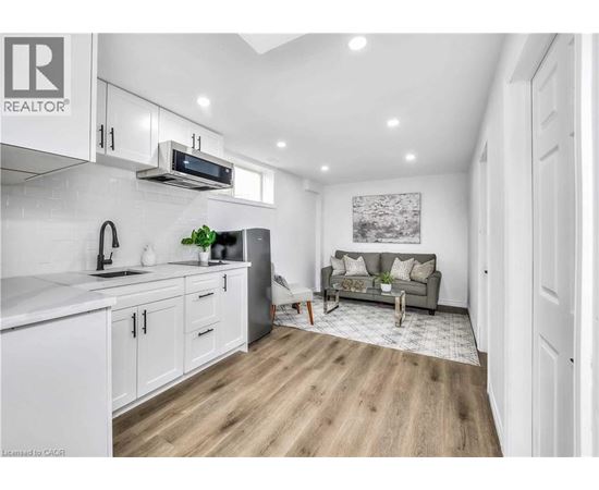 A well-lit kitchen with white cabinets and a grey sofa in the living room.