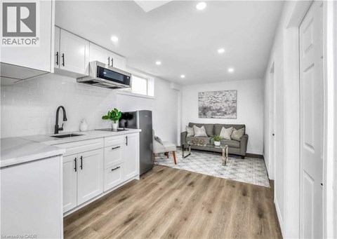 A well-lit kitchen with white cabinets and a grey sofa in the living room.