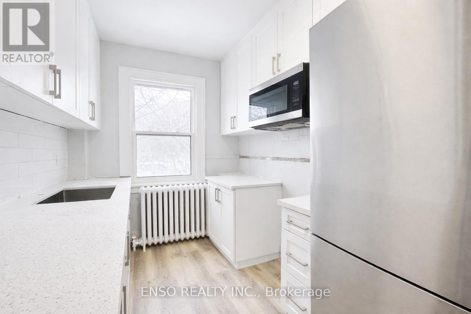 A white kitchen with a refrigerator, microwave, and a window.