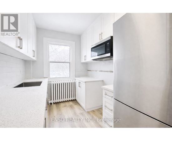 A white kitchen with a refrigerator, microwave, and a window.