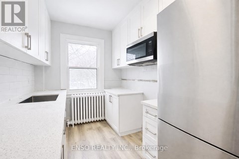 A white kitchen with a refrigerator, microwave, and a window.