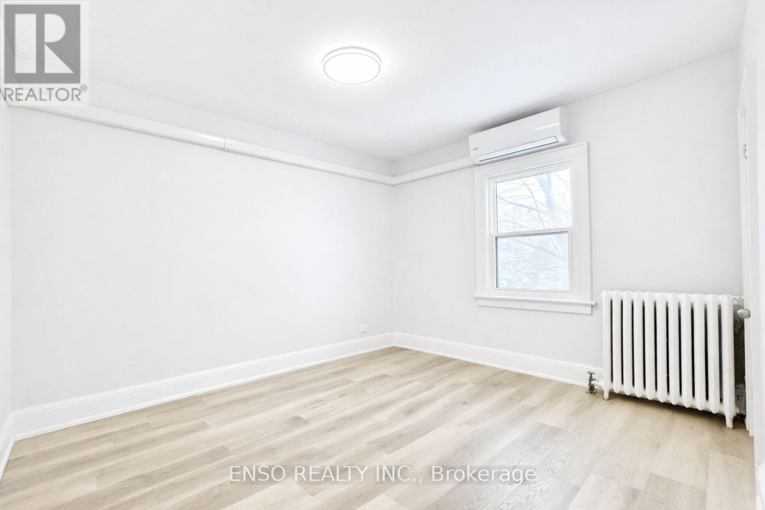 A white room with a window and a radiator on the floor.