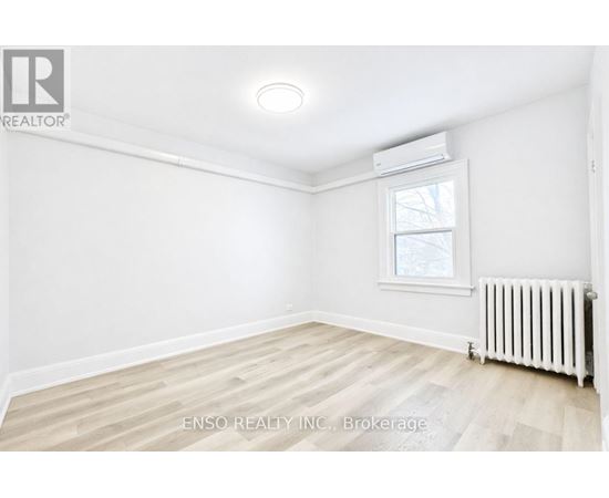 A white room with a window and a radiator on the floor.