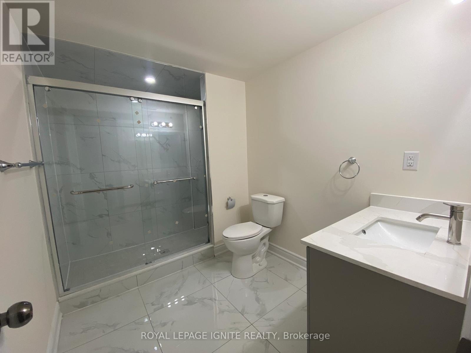 A bathroom with a glass shower door, toilet, and sink.