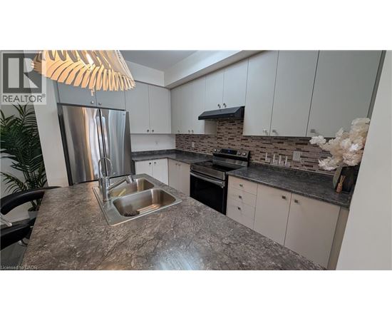 A kitchen with a granite countertop and a stainless steel refrigerator.