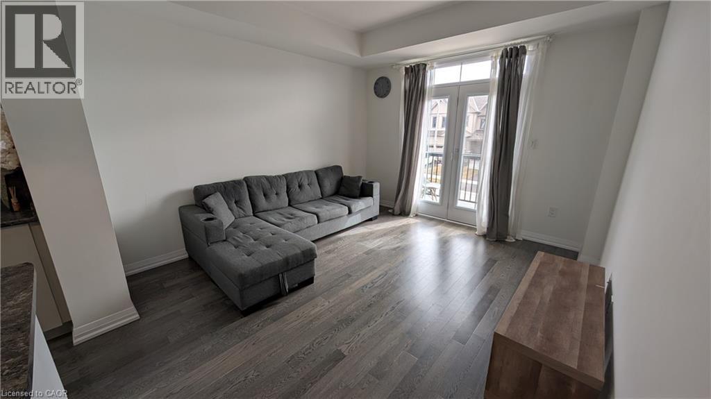 A grey couch in a room with wooden flooring and a window with curtains.