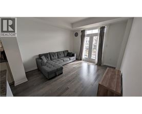 A grey couch in a room with wooden flooring and a window with curtains.