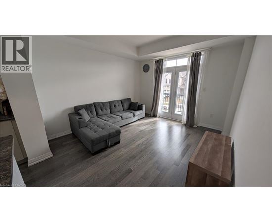 A grey couch in a room with wooden flooring and a window with curtains.