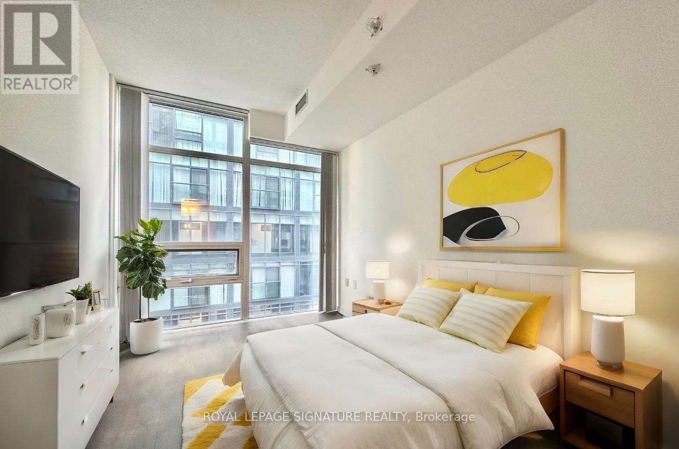 A bedroom with a large bed, a television, and a window overlooking a cityscape.