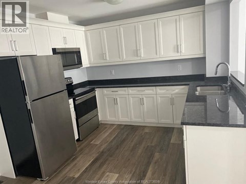 A kitchen with white cabinets and a black fridge.