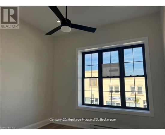 A room with a ceiling fan and a window showing a building outside.