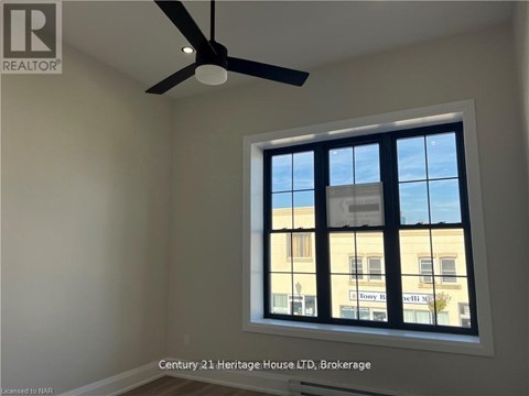 A room with a ceiling fan and a window showing a building outside.