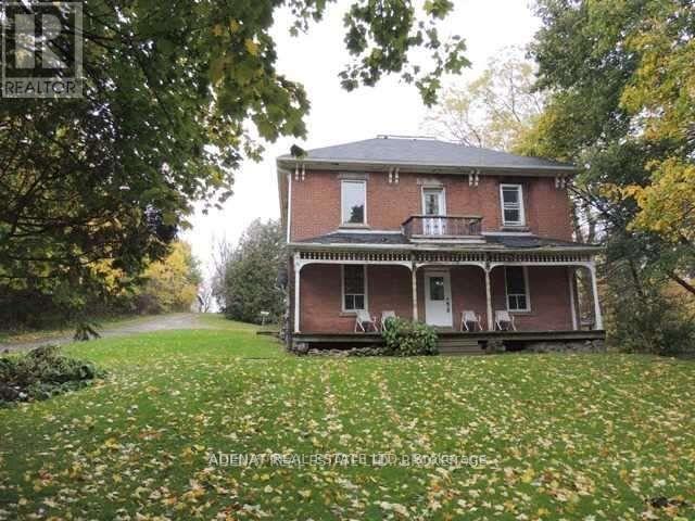 A house with a red brick exterior and a porch is surrounded by trees and grass.