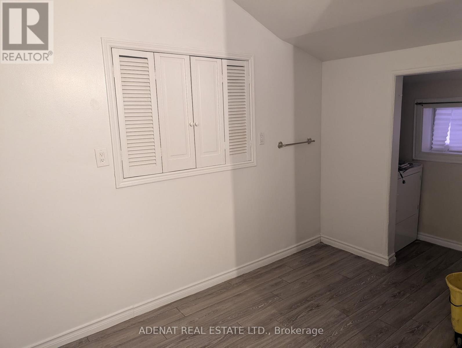 A room with white walls, a wooden floor, and a yellow bucket.