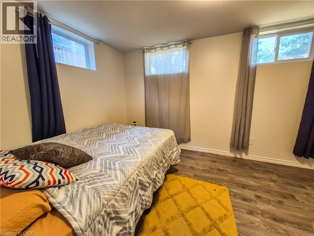 A bedroom with a bed, yellow rug, and two windows with curtains.