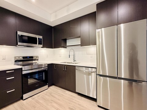 A modern kitchen with dark brown cabinets and stainless steel appliances.