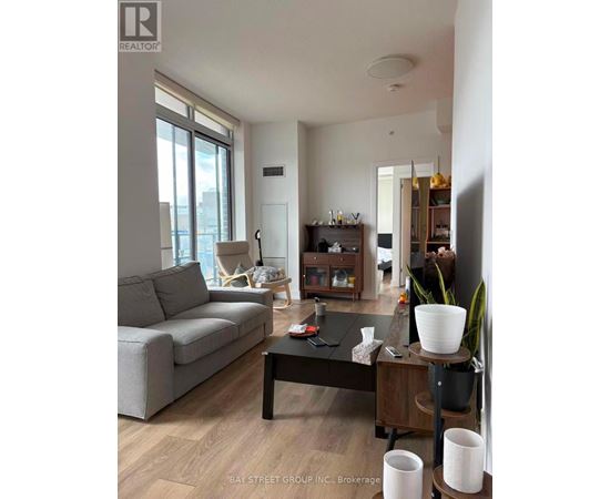 A living room with a grey couch, a black coffee table, and a wooden side table with a plant on it.