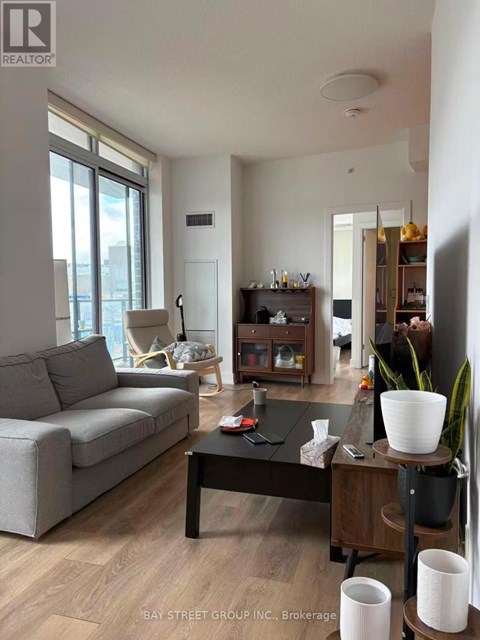 A living room with a grey couch, a black coffee table, and a wooden side table with a plant on it.