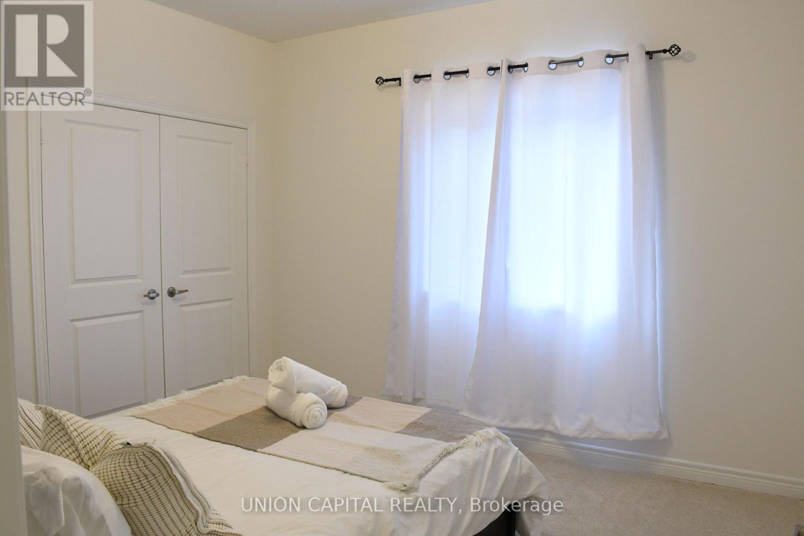A bedroom with a bed, a window with curtains, and a nightstand with a lamp.