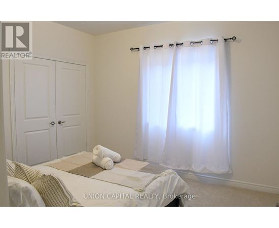 A bedroom with a bed, a window with curtains, and a nightstand with a lamp.