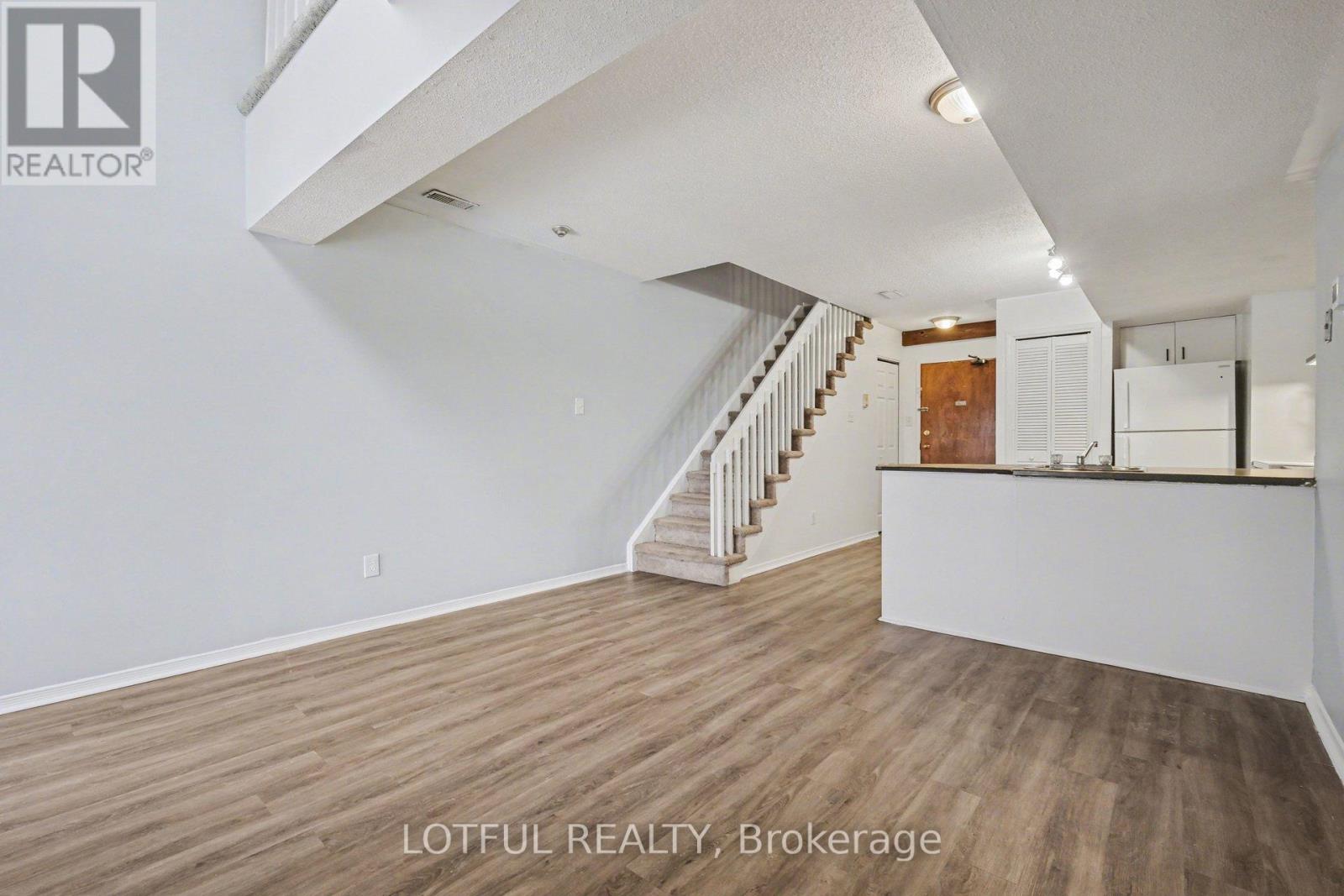 A spacious room with wooden flooring and a staircase leading to the upper level.