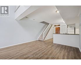 A spacious room with wooden flooring and a staircase leading to the upper level.