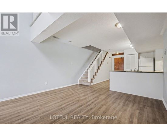 A spacious room with wooden flooring and a staircase leading to the upper level.
