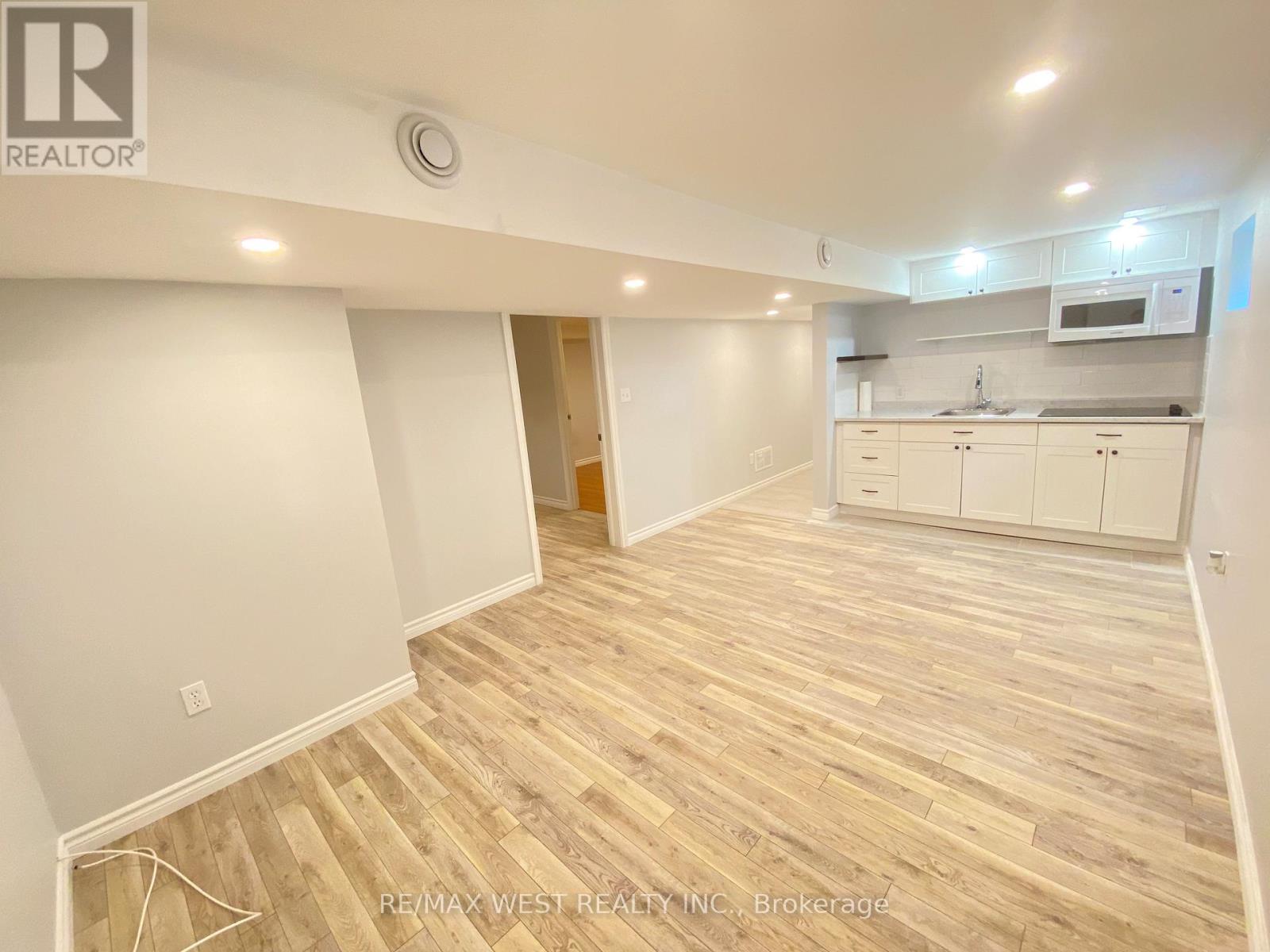 A spacious room with wooden flooring and white walls, featuring a kitchen area with white cabinets and appliances.