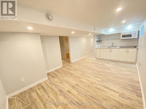 A spacious room with wooden flooring and white walls, featuring a kitchen area with white cabinets and appliances.
