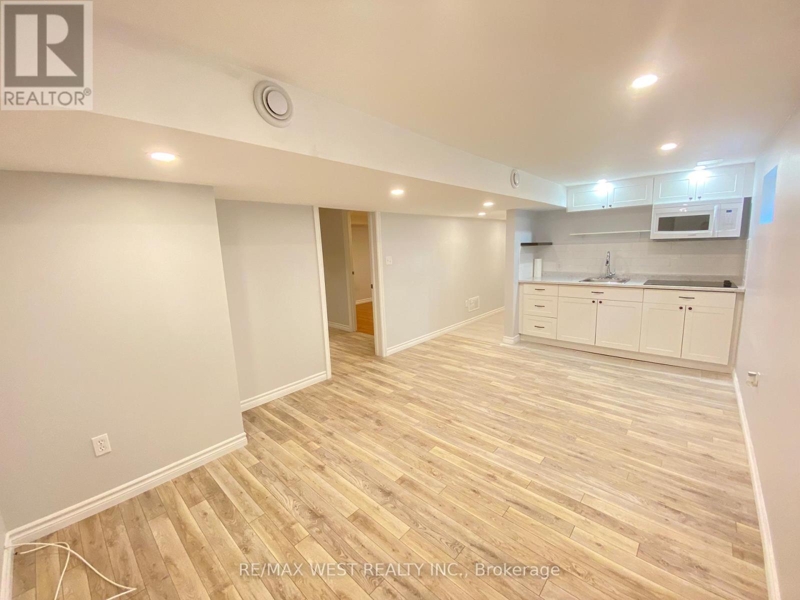A room with wooden flooring and a kitchen area in the background.