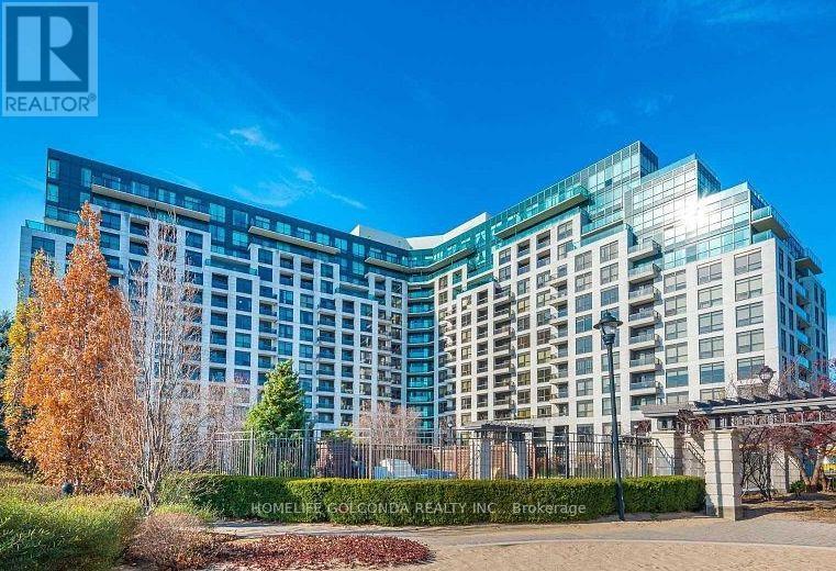 A modern multi-story building with a glass facade is surrounded by a well-maintained lawn and trees.