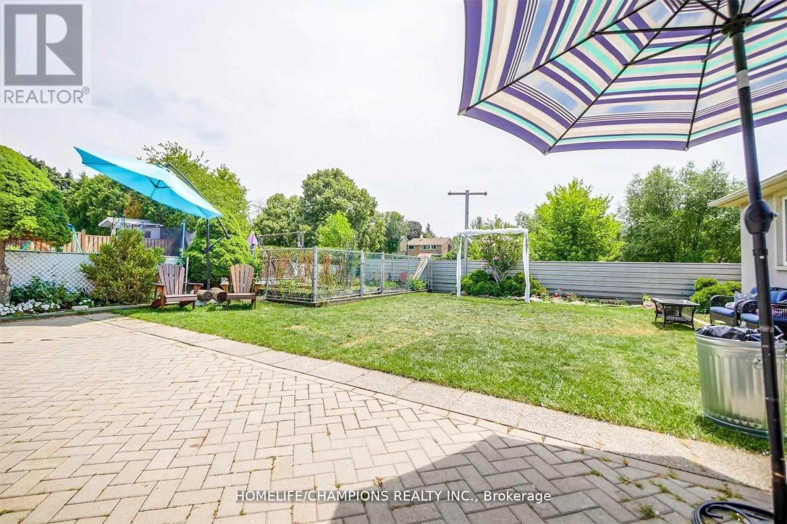 A patio with a brick pattern is surrounded by a grassy area and a fence.