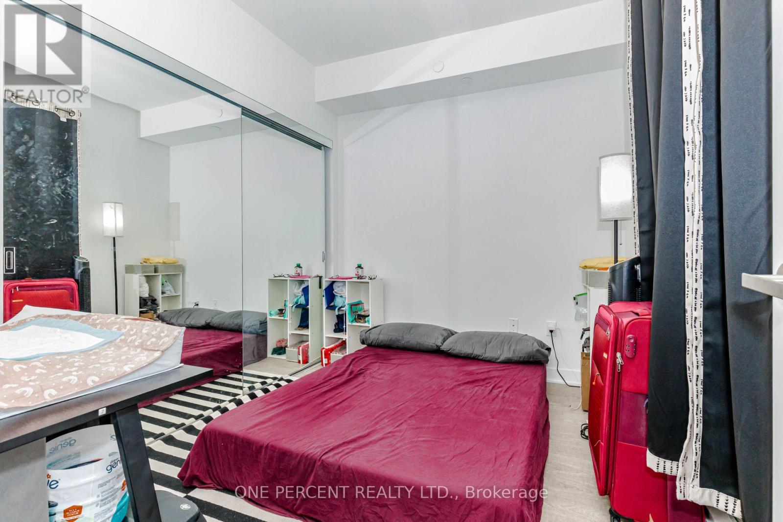 A bedroom with a red bedspread and a mirror on the wall.