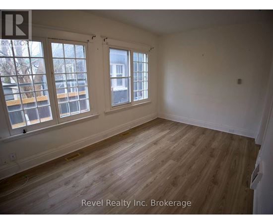 A room with wooden floors and white walls, with windows on the left side.