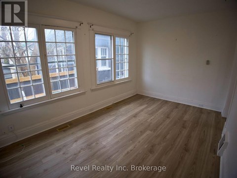 A room with wooden floors and white walls, with windows on the left side.