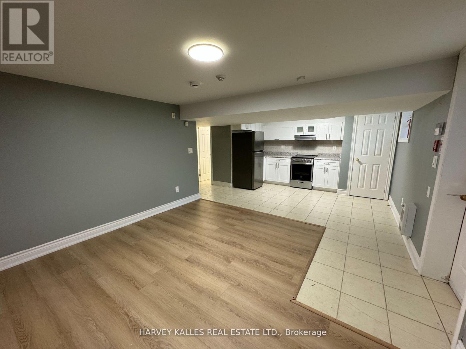 A spacious room with wooden flooring and a kitchen area in the background.