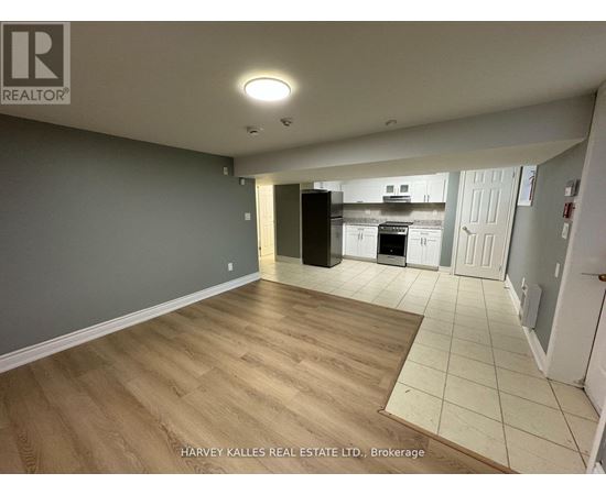 A spacious room with wooden flooring and a kitchen area in the background.