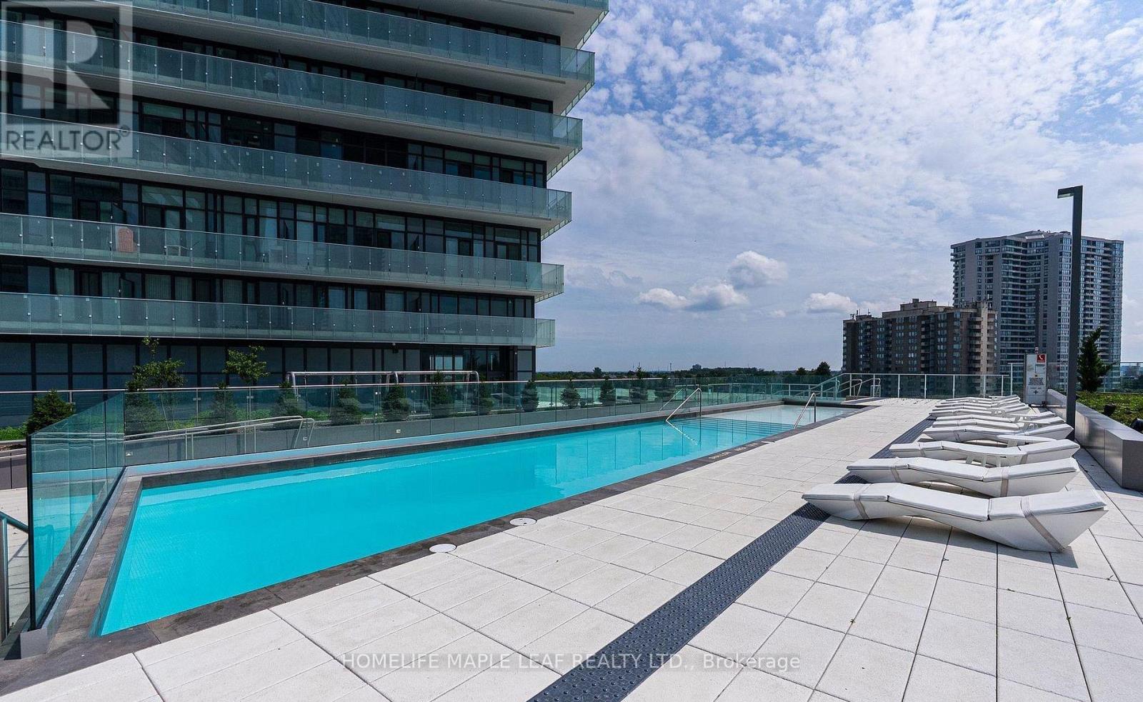A large swimming pool on a rooftop with a glass railing and a building in the background.