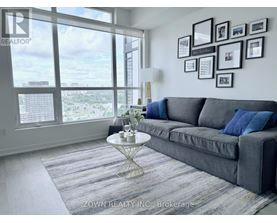 A living room with a grey couch, a round table, and a view of the city through the windows.