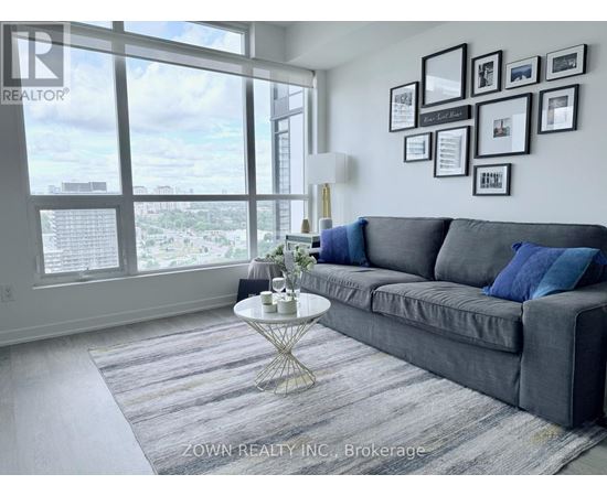 A living room with a grey couch, a round table, and a view of the city through the windows.
