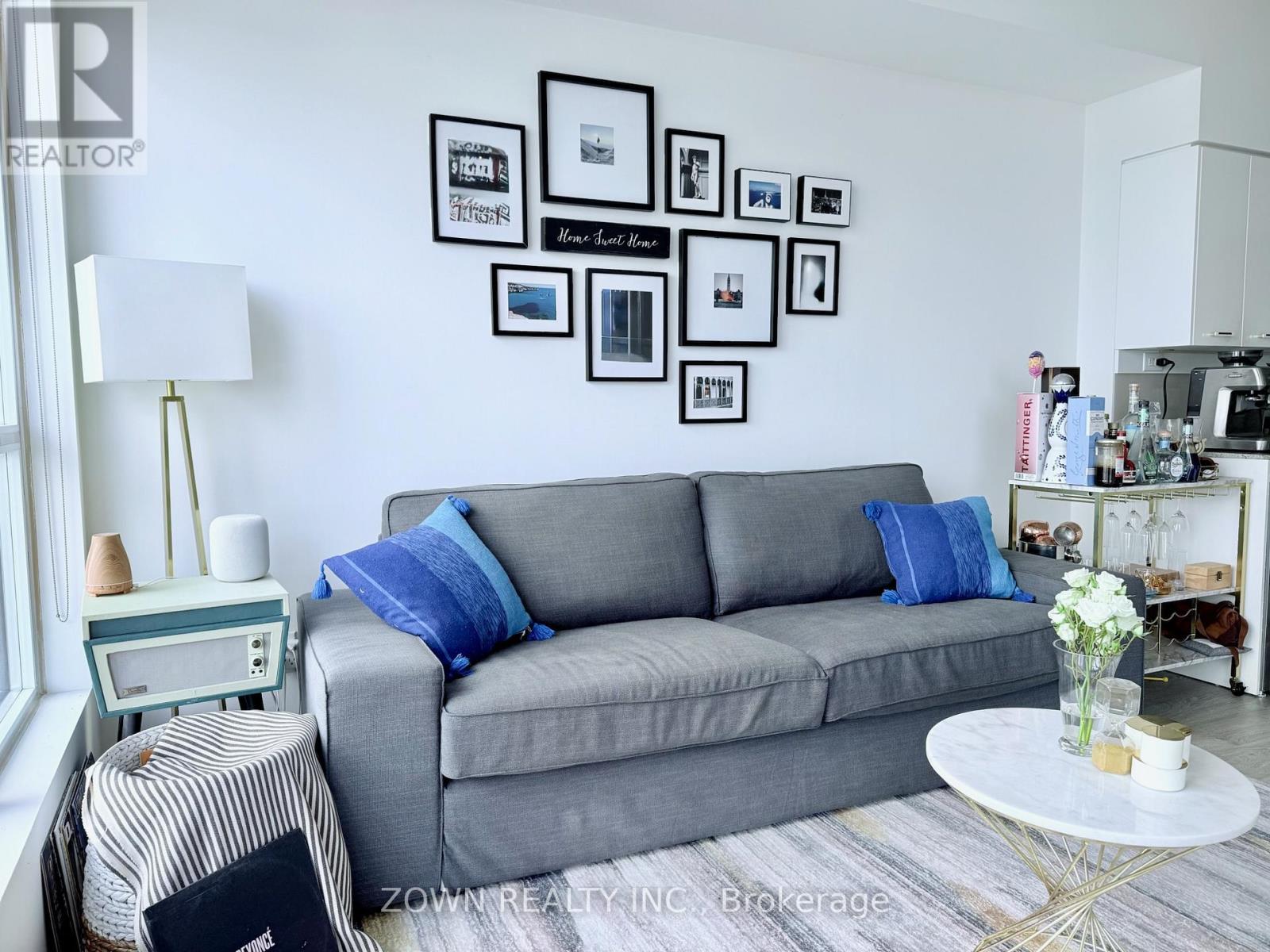 A grey couch with blue pillows sits in a living room with a white coffee table in front of it.