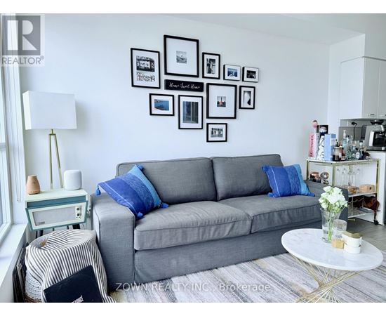 A grey couch with blue pillows sits in a living room with a white coffee table in front of it.