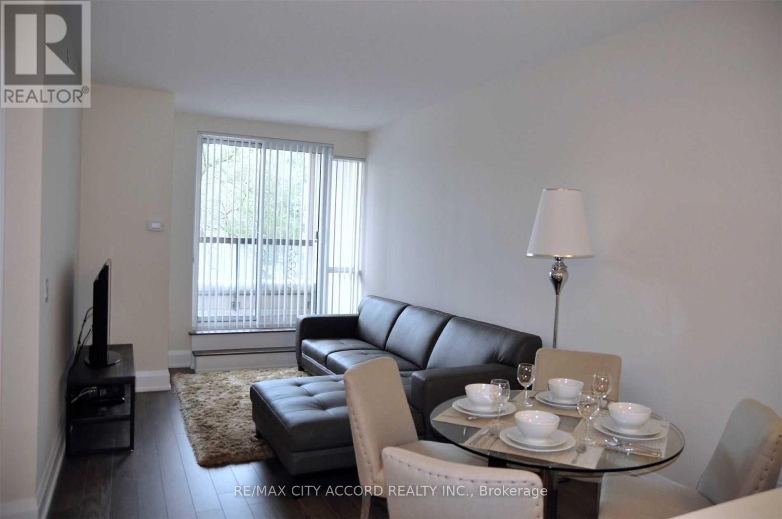 A living room with a black leather couch and a glass table with plates and glasses on it.