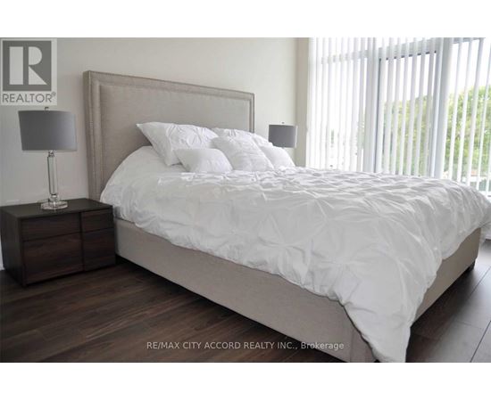 A bedroom with a large bed and a nightstand with a lamp.